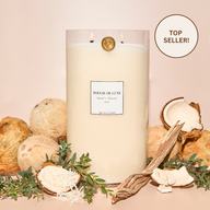 Santal & Coconut Big Ass Candle lit with coconuts and greenery surrounding it.