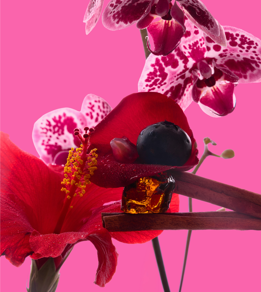 Amber-colored bottle with a black cap on a pink background with flowers