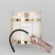 A gold-colored candle holder with a clear baby big ass candle on top and a pink long-ass lighter attached to the holder.
