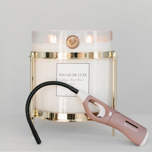 A gold-colored candle holder with a clear baby big ass candle on top and a pink long-ass lighter attached to the holder.