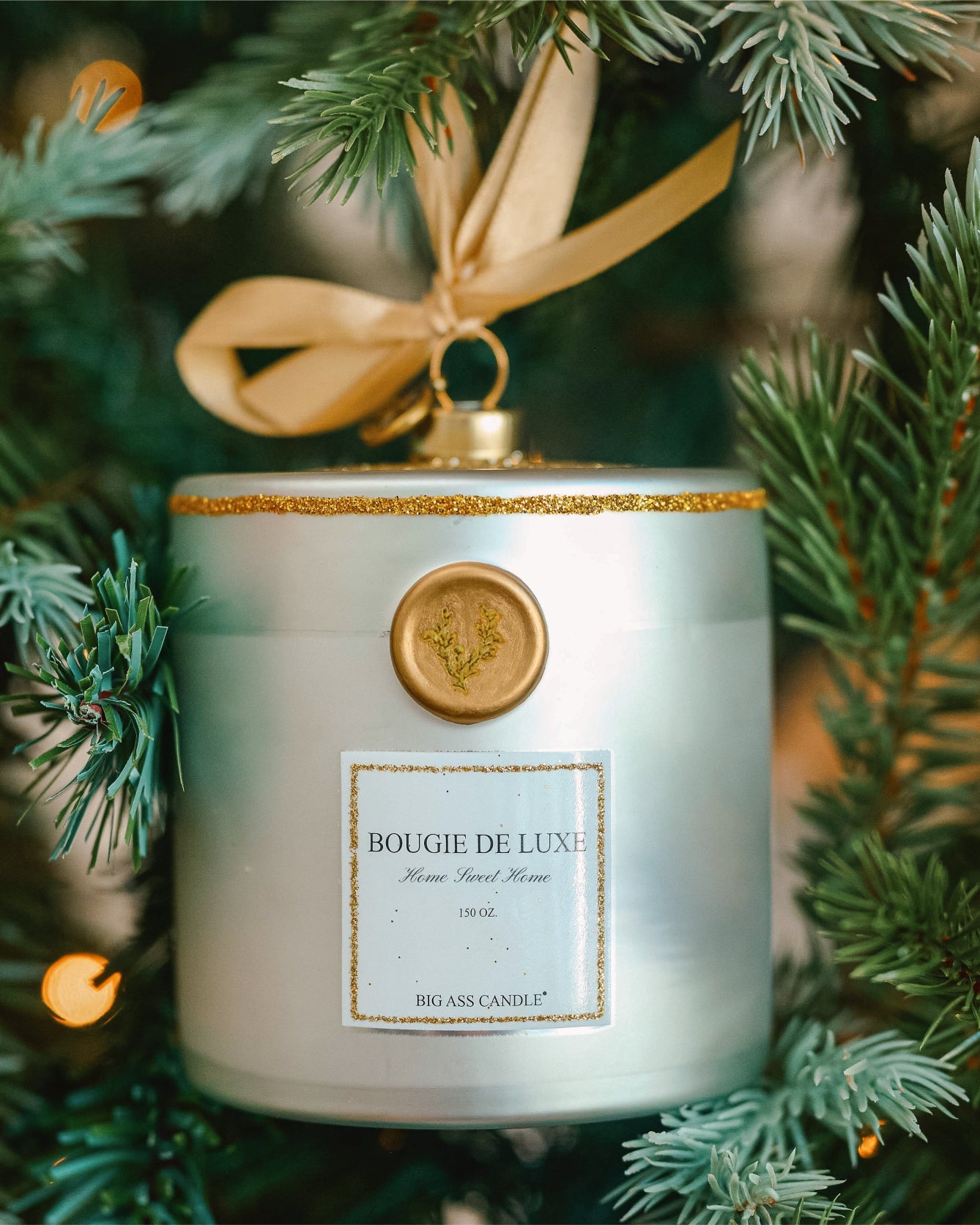 Bougie De Luxe candle ornament among Christmas tree branches with lights in the background