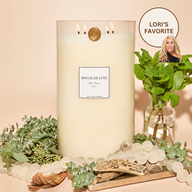 Lit Palo Santo Big Ass Candle with greenery and wood to represent scent notes surrounding it.
